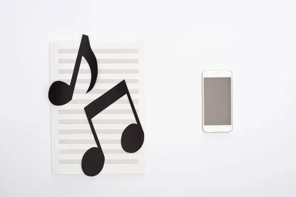 Visão superior de notas de corte de papel no livro de música perto do smartphone no fundo branco — Fotografia de Stock