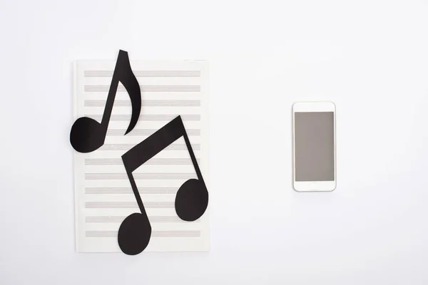 Top view of paper cut notes on music book near smartphone on white background — Stock Photo