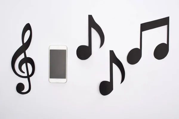 Top view of paper cut music notes with smartphone on white background — Stock Photo