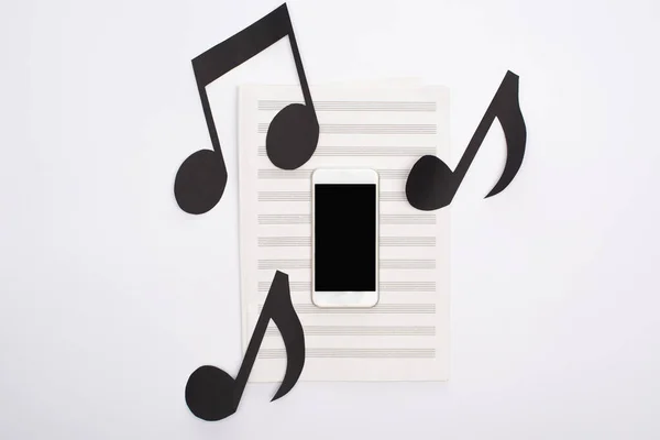 Visão superior do smartphone com notas de corte de papel no livro de música no fundo branco — Fotografia de Stock