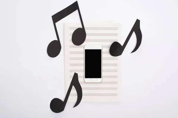 Top view of smartphone with paper cut notes on music book on white background — Stock Photo