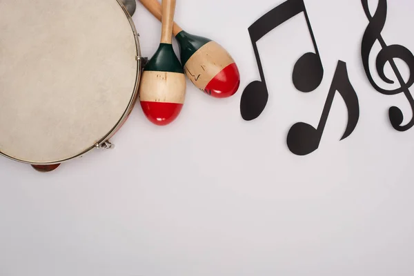 Vue du dessus des maracas en bois près du tambourin et du papier coupent des notes de musique sur fond blanc — Photo de stock