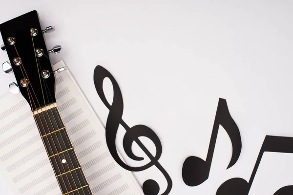 Vista superior de notas de corte de papel perto do livro de música e guitarra acústica no fundo branco — Fotografia de Stock