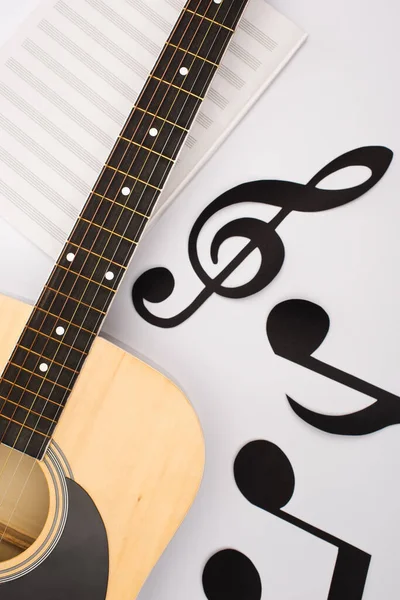 Vista superior de notas de papel cortadas cerca de libro de música con guitarra acústica sobre fondo blanco - foto de stock