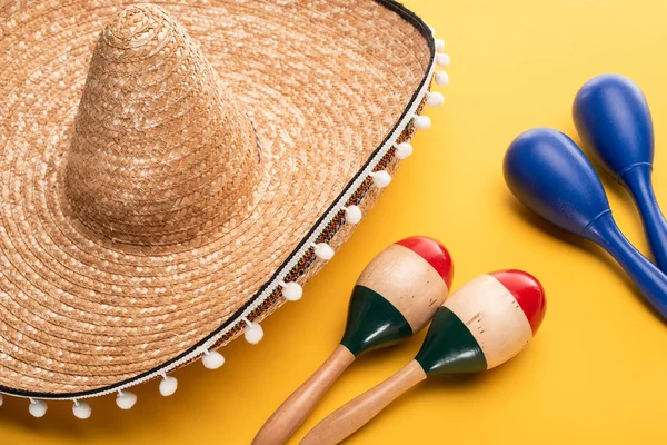 Maracas coloridas e azuis de madeira perto de sombrero no fundo amarelo — Fotografia de Stock