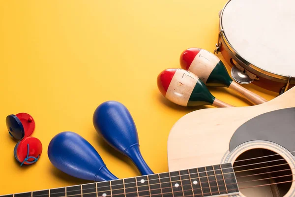 Maracas coloridas e azuis de madeira com tamborim, castanholas e violão sobre fundo amarelo — Fotografia de Stock