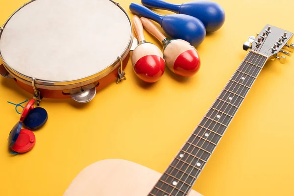 Bunte und blaue Maracas aus Holz, Tamburin, Kastagnetten und Akustikgitarre auf gelbem Hintergrund — Stockfoto