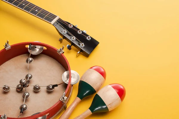 Tambourine near colorful wooden maracas and acoustic guitar on yellow background — Stock Photo