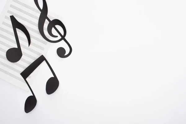 Vista dall'alto di note nere tagliate su carta su libro di musica su sfondo bianco — Foto stock