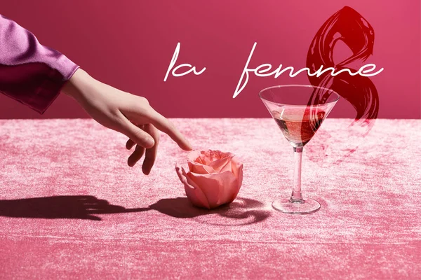 Abgeschnittene Ansicht einer Frau, die Rose in der Nähe von Glas mit Getränk auf Velourtuch berührt, isoliert auf rosa, la femme und Illustration vom 8. März — Stockfoto