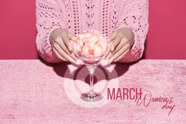 Vista recortada de la mujer con pétalos en vidrio sobre tela de terciopelo aislado en rosa, ilustración 8 marzo - foto de stock