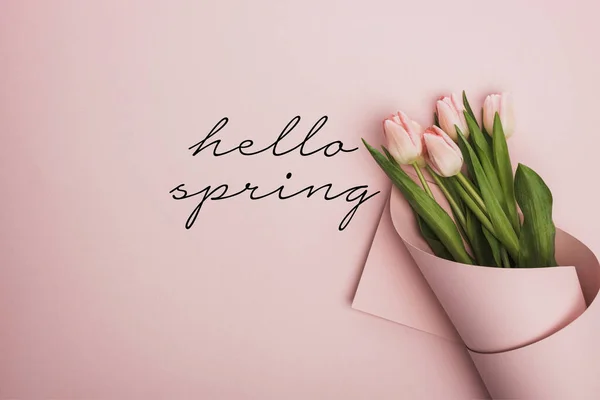 Vue du dessus des tulipes enveloppées dans du papier sur fond rose, illustration du printemps bonjour — Photo de stock