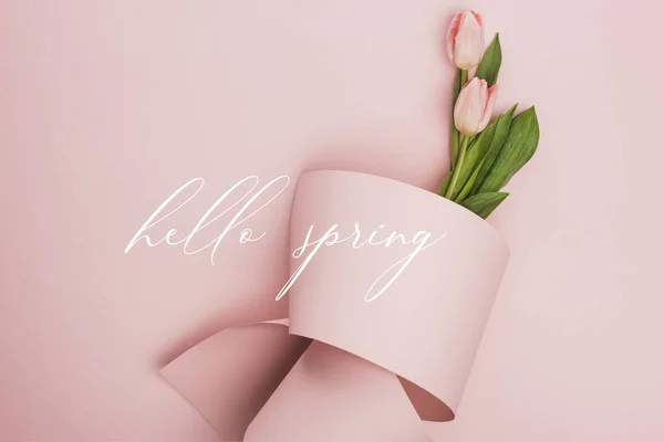 Vue du dessus des tulipes enveloppées dans du papier sur fond rose, illustration du printemps bonjour — Photo de stock