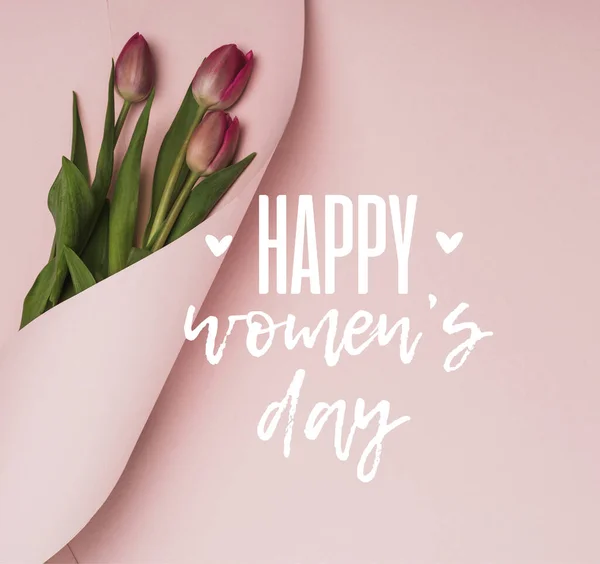 Top view of purple tulips wrapped in paper on pink background, happy womens day illustration — Stock Photo