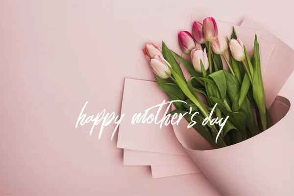 Vue du dessus des tulipes printanières enveloppées dans du papier sur fond rose, illustration heureuse de la fête des mères — Photo de stock