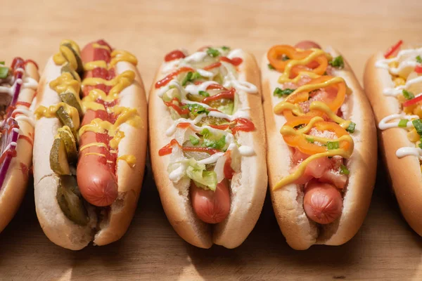 Deliciosos cachorros-quentes frescos com molhos na mesa de madeira — Fotografia de Stock