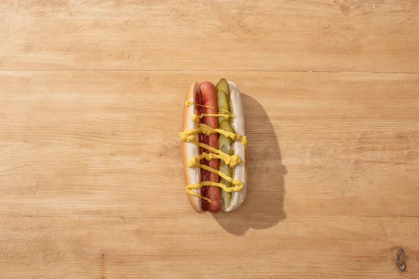 Top view of delicious hot dog with pickles, mustard and ketchup on wooden table — Stock Photo
