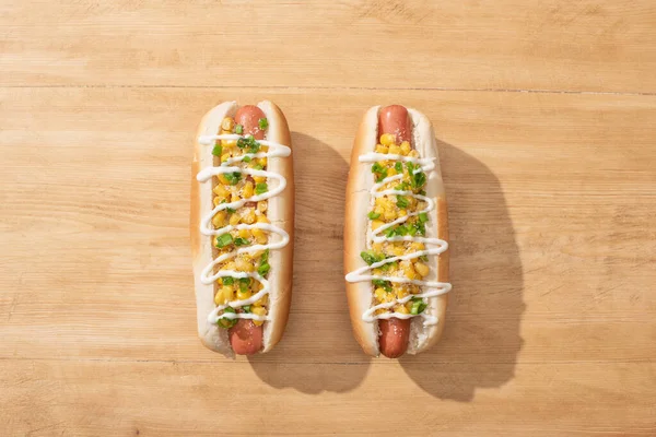 Blick von oben auf köstliche Hotdogs mit Mais, grünen Zwiebeln und Mayonnaise auf Holztisch — Stockfoto