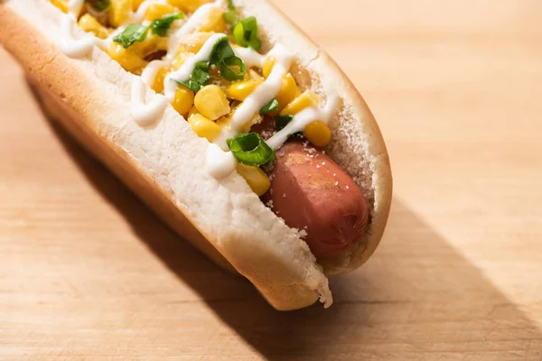 Vista de cerca de un delicioso perrito caliente con maíz, cebolla verde y mayonesa en la mesa de madera - foto de stock