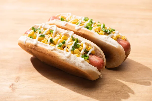 Deliciosos cachorros-quentes com milho, cebola verde e maionese na mesa de madeira — Fotografia de Stock