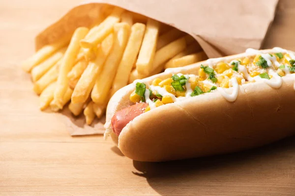 Foyer sélectif de délicieux hot dog avec maïs, oignon vert et mayonnaise près des frites sur table en bois — Photo de stock