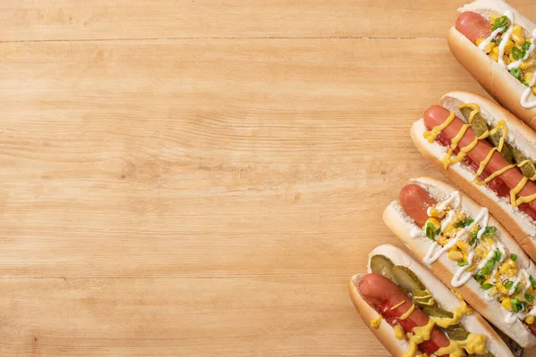 Blick von oben auf köstliche Hotdogs mit Mais, grünen Zwiebeln und Essiggurken auf Holztisch — Stockfoto