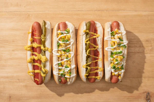 Flat lay with delicious hot dogs with corn, green onion and pickles on wooden table — Stock Photo