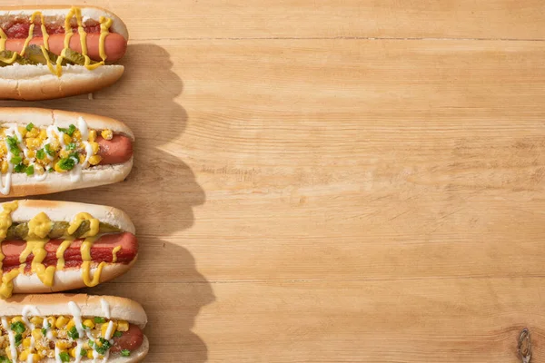 Vista superior de deliciosos hot dogs con maíz, cebolla verde y encurtidos en mesa de madera - foto de stock
