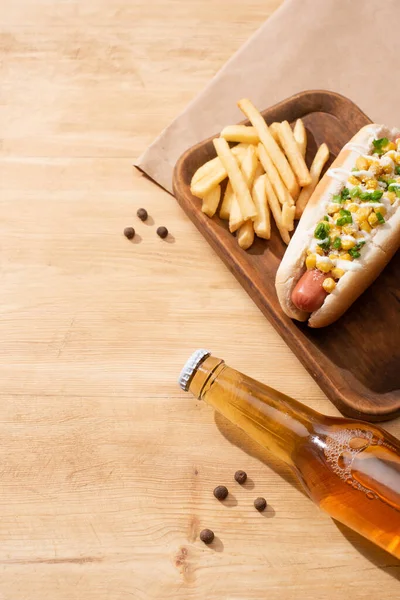 Delicioso cachorro-quente com milho, cebola verde e maionese perto de cerveja e batatas fritas na mesa de madeira — Fotografia de Stock