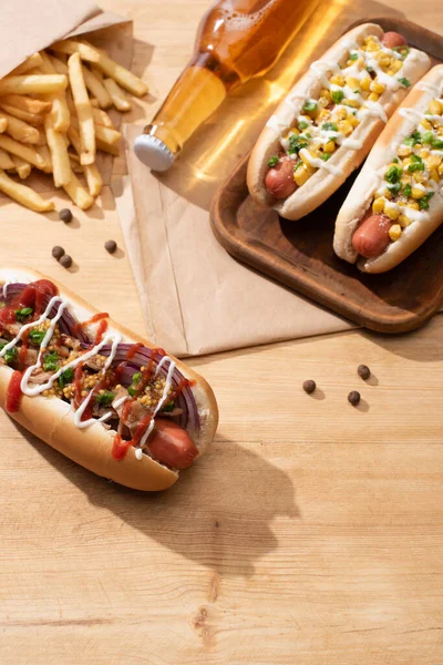 Deliciosos cachorros-quentes perto de cerveja e batatas fritas na mesa de madeira — Fotografia de Stock