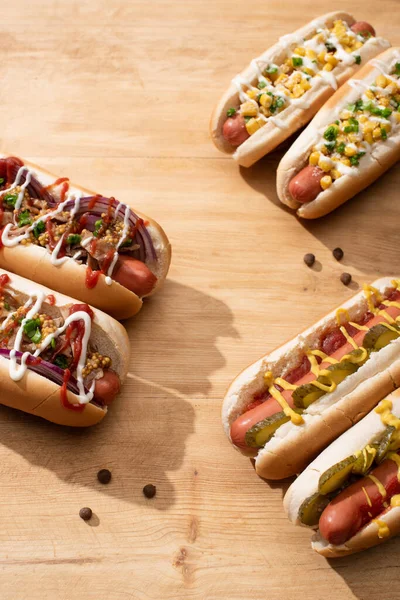 Deliciosos cachorros-quentes com cebola vermelha, bacon, picles e milho na mesa de madeira — Fotografia de Stock