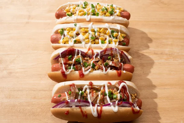 Deliciosos cachorros-quentes com cebola vermelha, bacon e milho na mesa de madeira — Fotografia de Stock