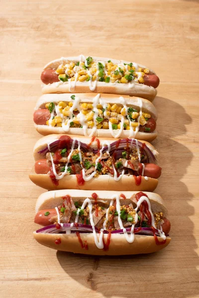 Deliciosos cachorros-quentes com cebola vermelha, bacon e milho na mesa de madeira — Fotografia de Stock