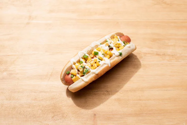Delicioso hot dog con maíz, cebolla verde y mayonesa sobre mesa de madera - foto de stock