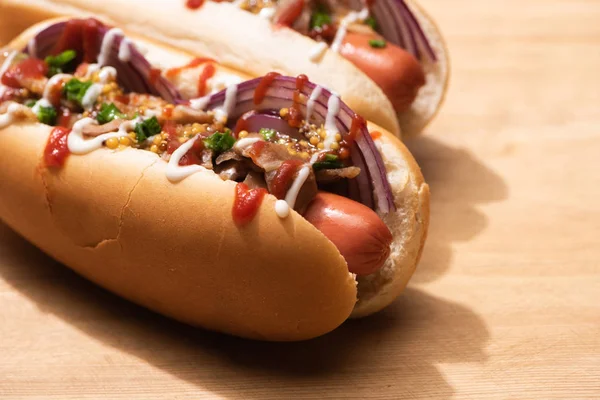 Selective focus of delicious hot dogs with red onion, bacon and Dijon mustard on wooden table — Stock Photo