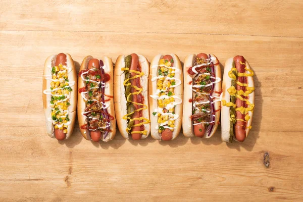 Blick von oben auf verschiedene leckere Hot Dogs mit Gemüse und Soßen auf Holztisch — Stockfoto