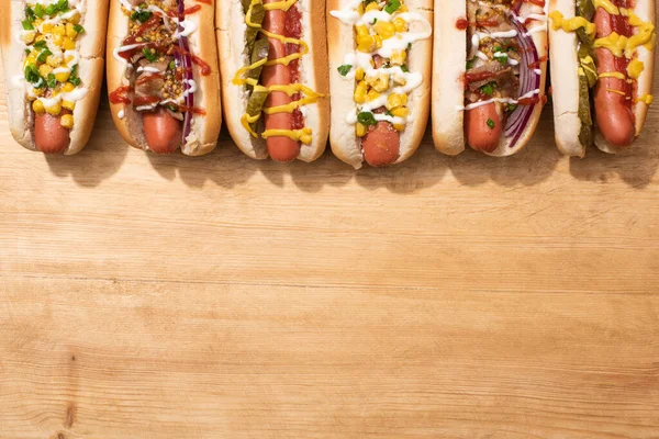 Vista superior de vários cachorros-quentes deliciosos com legumes e molhos na mesa de madeira — Fotografia de Stock