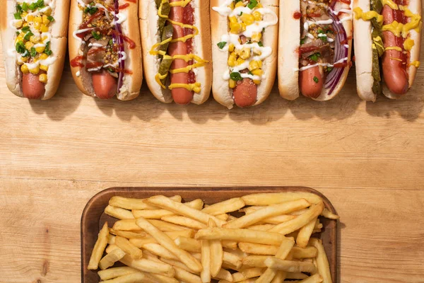 Top view of various delicious hot dogs with vegetables and sauces near french fries on wooden table — Stock Photo