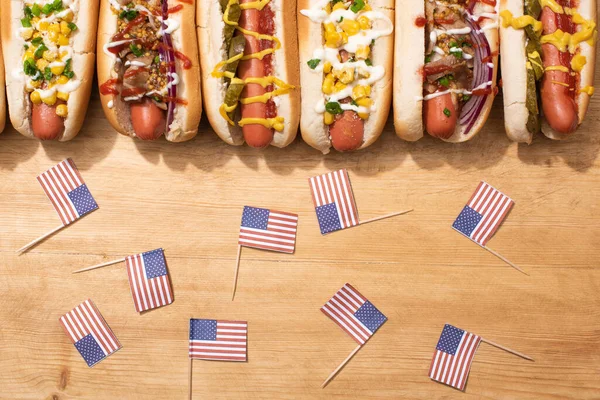 Top view of various delicious hot dogs with vegetables and sauces near american flags on wooden table — Stock Photo