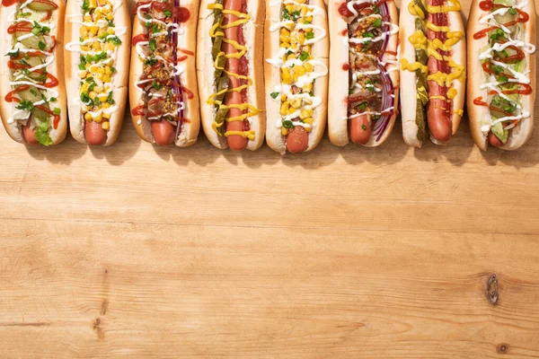 Blick von oben auf verschiedene leckere Hot Dogs mit Gemüse und Soßen auf Holztisch — Stockfoto