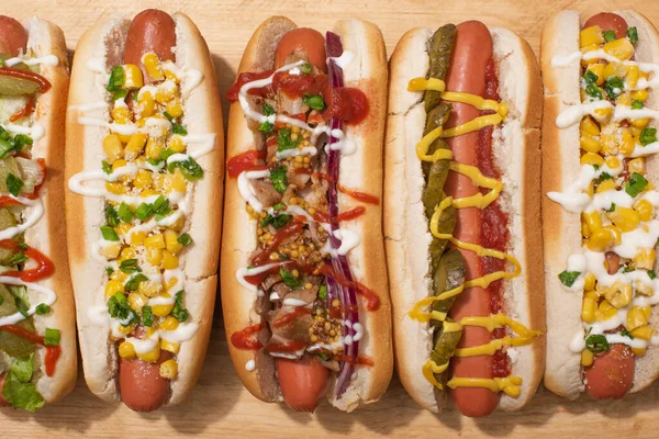 Blick von oben auf verschiedene leckere Hot Dogs mit Gemüse und Soßen auf Holztisch — Stockfoto