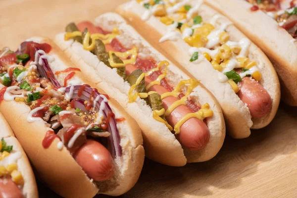 Varios perros calientes deliciosos con verduras y salsas en la mesa de madera - foto de stock