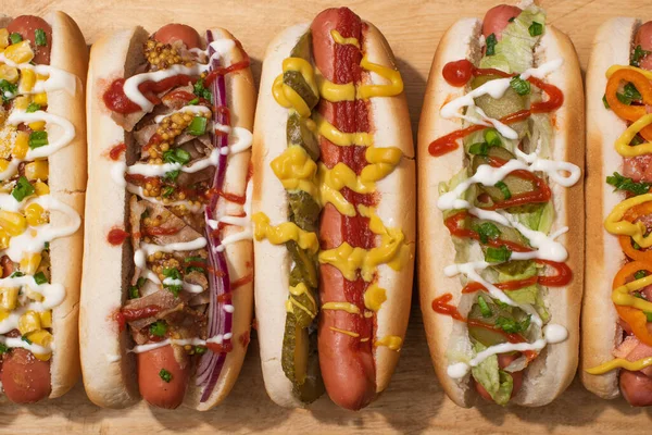 Vista superior de varios perros calientes deliciosos con verduras y salsas en la mesa de madera - foto de stock