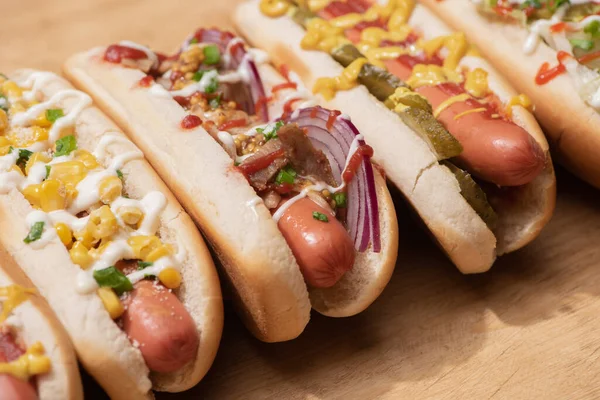 Vários cachorros-quentes deliciosos com legumes e molhos na mesa de madeira — Fotografia de Stock