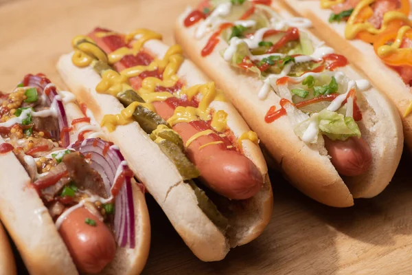 Various delicious hot dogs with vegetables and sauces on wooden table — Stock Photo