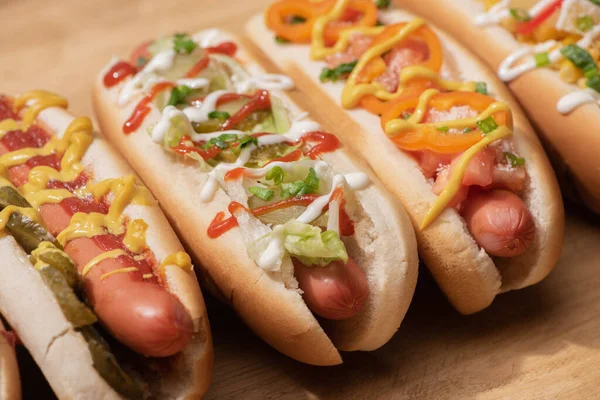 Fresh various delicious hot dogs with vegetables and sauces on wooden table — Stock Photo