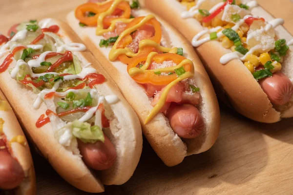 Fresco vários cachorros-quentes deliciosos com legumes e molhos na mesa de madeira — Fotografia de Stock