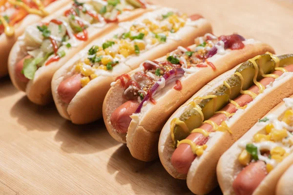 Foco seletivo de vários cachorros-quentes deliciosos frescos com legumes e molhos na mesa de madeira — Fotografia de Stock