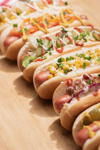 Enfoque selectivo de varios perros calientes deliciosos frescos con verduras y salsas en la mesa de madera - foto de stock