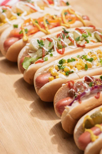 Selective focus of fresh various delicious hot dogs with vegetables and sauces on wooden table — Stock Photo